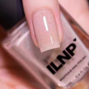May include: A close-up of a fingernail painted with a light pink nail polish with a subtle shimmer. The nail polish bottle is in the background and says "ILNP" on the label.