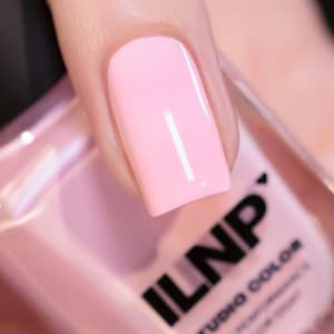 May include: A close-up of a pink nail polish bottle with the brand name "ILNP" printed on the label. The bottle is partially obscured by a finger with a pink nail painted with the polish.
