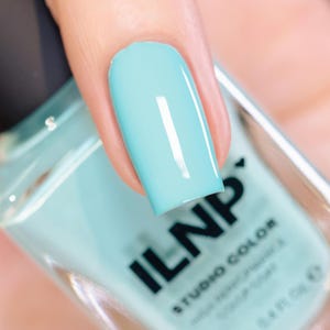 May include: A close-up of a fingernail painted with a bright, glossy, light blue nail polish. The nail polish bottle is in the background, with the brand name "ILNP" and "Studio Color" visible.