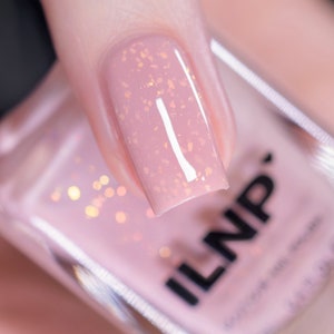 Könnte beinhalten: Nahaufnahme eines hellrosa Nagellacks mit schimmerndem Finish. Die Flasche ist mit "ILNP" beschriftet und ist teilweise im Bild zu sehen.