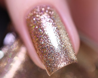 Puede incluir: Primer plano de una uña pintada con esmalte de uñas dorado con purpurina. La uña tiene una forma ovalada clara y el esmalte tiene un aspecto brillante y texturizado. El fondo está borroso, lo que sugiere un enfoque en la uña y el esmalte.