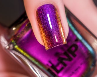May include: A close-up of a fingernail painted with a holographic purple and gold nail polish. The nail polish bottle is in the background and says "ILNP" on the label.