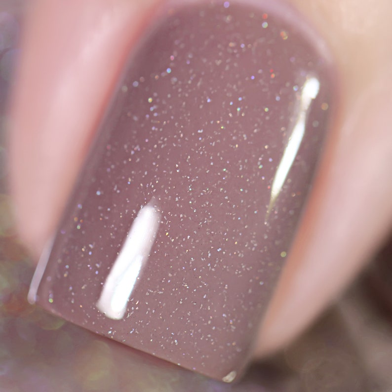 Peut inclure: Gros plan sur un vernis &agrave; ongles brun clair avec une finition chatoyante. Le vernis a une brillance subtile et une texture lisse et brillante.
