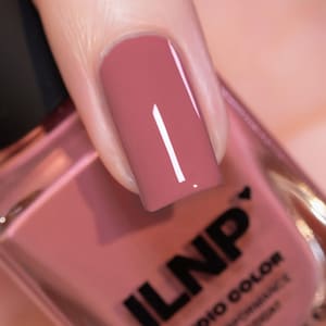May include: Close-up of a fingernail painted with a dusty rose nail polish. The nail polish is glossy and reflects light. The bottle of nail polish is partially visible, with the brand name "ILNP" in black letters.