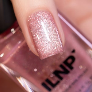 May include: A close-up of a pink nail polish bottle with a glittery pink nail polish applied to a fingernail. The bottle is labeled "ILNP".