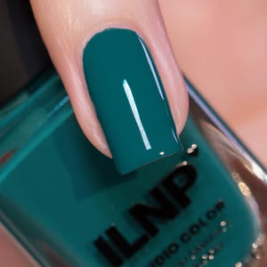 May include: Close-up of a fingernail painted with a glossy teal nail polish. The nail polish is a deep, saturated teal color. The bottle of nail polish is visible in the background, with the brand name "ILNP STUDIO COLOR" printed on it.
