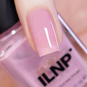 May include: A close-up of a pink nail polish bottle with a light pink nail polish with a shimmer finish. The bottle is labeled "ILNP".