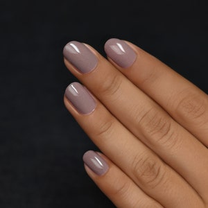 Peut inclure: Gros plan sur une main avec quatre ongles peints d'un vernis &agrave; ongles mauve clair.