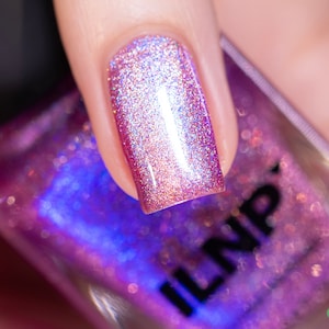 May include: A close-up of a pink nail polish with a holographic finish. The polish is applied to a fingernail and the bottle is visible in the background. The bottle is labeled "ILNP".