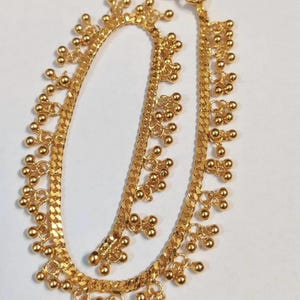 May include: A gold-colored anklet with a chain-like design. The anklet features small, round, gold-colored beads clustered together at intervals along the chain. The anklet is approximately 10 inches long and has a clasp closure.