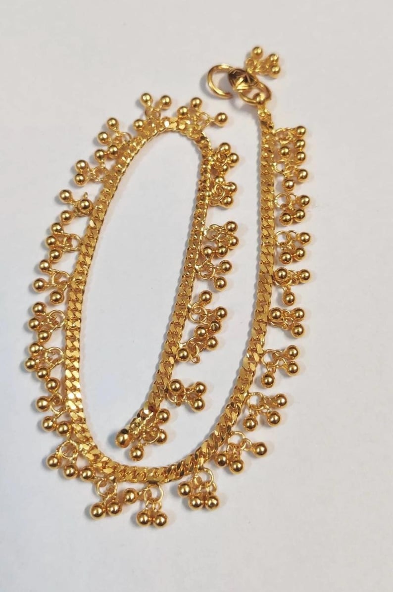 May include: A gold-colored anklet with a chain-like design. The anklet features small, round, gold-colored beads clustered together at intervals along the chain. The anklet is approximately 10 inches long and has a clasp closure.