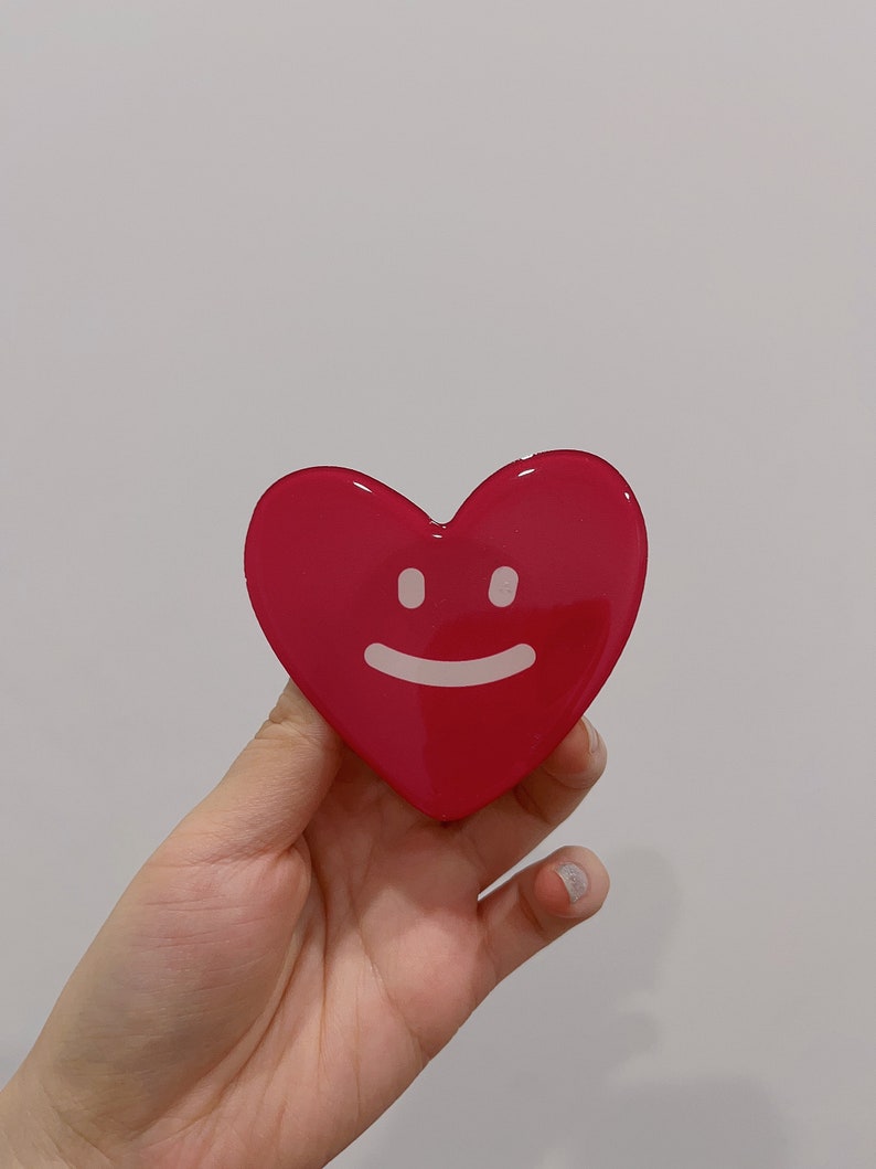 May include: A bright pink heart-shaped resin ornament with a white smiling face.