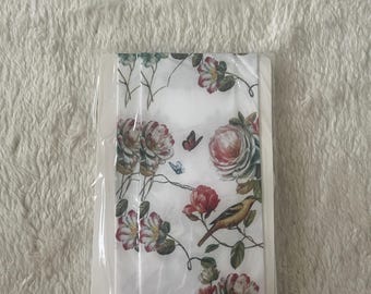 May include: A white fabric ribbon featuring a repeating pattern of red and pink roses, green leaves, small brown birds, and tiny butterflies. The ribbon is folded and encased in a clear plastic sleeve, displaying a detailed botanical illustration.