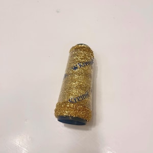 May include: A spool of gold glitter thread with a blue label that says "Kreinik" with a crown above the word.