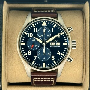 Puede incluir: Un reloj de pulsera de acero inoxidable con esfera azul oscuro, n&uacute;meros y agujas blancos. El reloj tiene una correa de cuero marr&oacute;n y se muestra en una caja beige. La esfera del reloj incluye el texto "IWC SCHAFFHAUSEN".