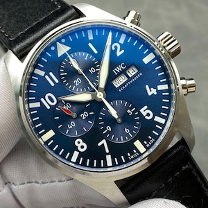 Puede incluir: Un reloj IWC Schaffhausen de acero inoxidable con esfera azul y correa de cuero negro. La esfera del reloj presenta n&uacute;meros blancos, tres subesferas y la visualizaci&oacute;n del d&iacute;a y la fecha. El reloj es de estilo cron&oacute;grafo.