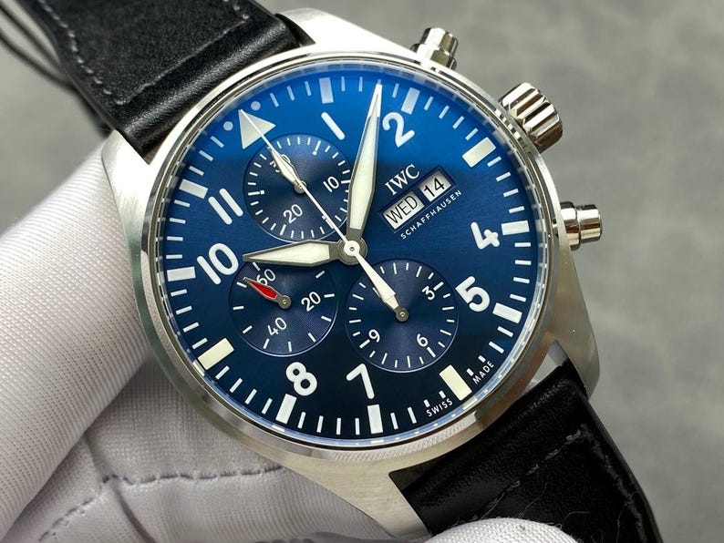 Puede incluir: Un reloj IWC Schaffhausen de acero inoxidable con esfera azul y correa de cuero negro. La esfera del reloj presenta n&uacute;meros blancos, tres subesferas y la visualizaci&oacute;n del d&iacute;a y la fecha. El reloj es de estilo cron&oacute;grafo.