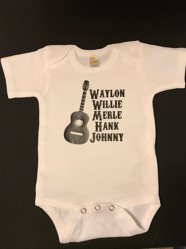 May include: White baby onesie with a black silhouette of a guitar and the names Waylon, Willie, Merle, Hank, and Johnny printed vertically.