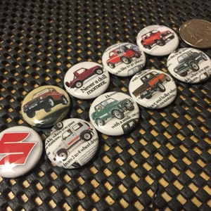 May include: A collection of nine round, white button pins with colorful images and text. The pins feature a red, white, and blue Suzuki logo, a red Suzuki vehicle, a green Suzuki vehicle, and a white Suzuki vehicle. The text on the pins includes "Never a dull moment", "with a smile on your face", "hoot and holler when you pass stations", and "from 2 to 4 wheel drive".
