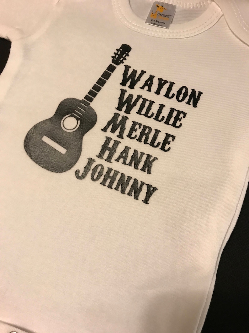 May include: White baby onesie with a black silhouette of a guitar and the names Waylon, Willie, Merle, Hank, and Johnny printed in black.