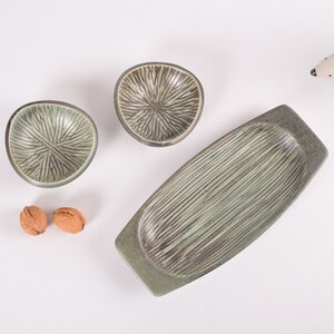 May include: A set of three green ceramic serving dishes. The dishes have a textured, striped design. Two of the dishes are small and round, while the third is larger and rectangular.