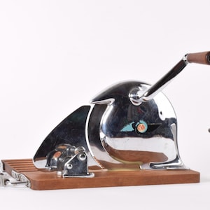 Puede incluir: Una exprimidora de cítricos cromada vintage con base y mango de madera. La exprimidora tiene un diseño único y está acompañada de un pequeño limón y una figura de oso polar blanco. Es una herramienta de cocina.