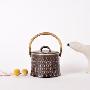 Puede incluir: Un azucarero de cerámica marrón con un asa tejida y un patrón geométrico. El tazón está sobre una superficie blanca.