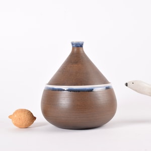 May include: A brown ceramic jar with a white and blue rim. The jar has a rounded, teardrop shape.