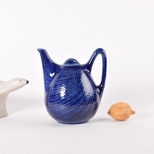 Puede incluir: Una tetera de cerámica azul con una figurita de oso polar blanco y un limón marrón sobre un fondo blanco.