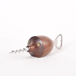 May include: A wooden bottle opener shaped like a narwhal with a silver corkscrew and bottle opener.
