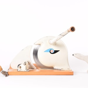 Puede incluir: Cortador de limones vintage blanco y madera con diseño de ave estilizada, una pequeña figura de oso polar blanco y un limón. El cortador tiene una cuchilla circular y un mango. Una herramienta de cocina única.