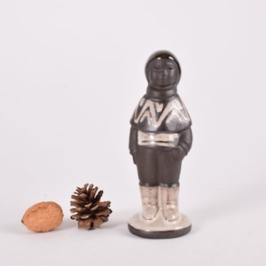 May include: A ceramic figurine of a person wearing a black and white patterned sweater and black trousers. The figurine is standing on a white base.