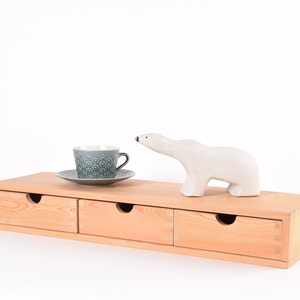 May include: A wooden drawer unit with three drawers, a white ceramic polar bear figurine, and a blue and white teacup and saucer on top.