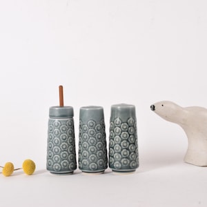 Può includere: Tre saliere e pepiere in ceramica con un motivo geometrico blu e bianco. Le saliere sono disposte in fila su una superficie bianca.