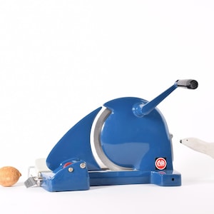 Puede incluir: Una cortadora de alimentos azul vintage con un mango negro y una cuchilla blanca. Un pequeño limón y una figura de oso polar blanco están junto a la cortadora. La cortadora tiene el texto "EVA".