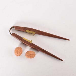 Puede incluir: Un cascanueces de madera con detalles de latón. El cascanueces está abierto y hay dos nueces a su lado.