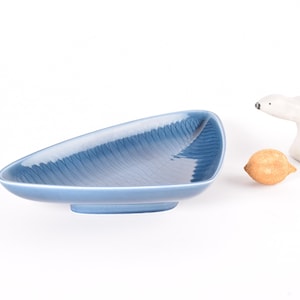 May include: A blue ceramic serving dish with a distinctive shape and textured interior. A small lemon and a white polar bear figurine are also present.