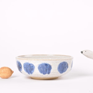 May include: A ceramic bowl with a white base and blue abstract designs. A small orange lemon-shaped figurine and a white polar bear figurine are next to the bowl. The bowl is approximately 8 inches in diameter.