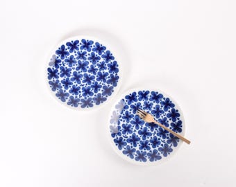 May include: Two white ceramic plates with a blue floral pattern. One plate has a gold fork resting on it. The plates are round and have a simple, elegant design, ideal for serving food.