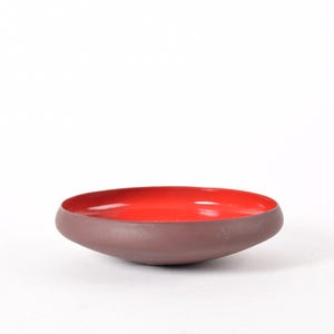 May include: A small, red and brown ceramic bowl with a rounded, slightly flared rim.