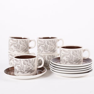 May include: Set of six white ceramic teacups and saucers with a brown rim and a grey floral pattern.