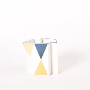 Könnte beinhalten: Eine weiße Keramikvase mit geometrischem Design mit gelben und blauen Dreiecken.