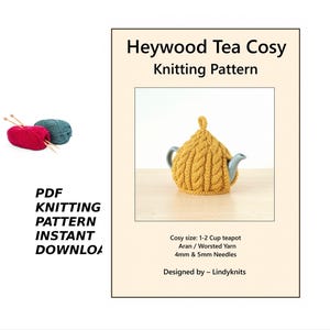 May include: A mustard-yellow knitted tea cosy with a cable knit pattern, covering a teapot. The image also shows balls of red and teal yarn with knitting needles, and text that reads "Heywood Tea Cosy Knitting Pattern".