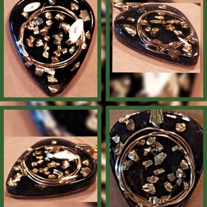May include: A black guitar pick pendant with gold flecks and a gold wire wrapped around it. The pendant is on a chain.