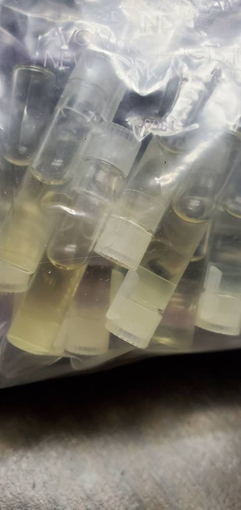 May include: A clear plastic bag filled with many small, clear glass bottles with white caps. The bottles are filled with a clear liquid.