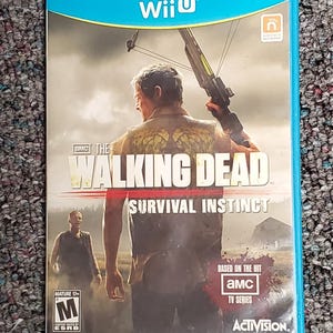 May include: A Wii U game case for "The Walking Dead: Survival Instinct." The cover features a man holding a crossbow, with the game's title and the AMC TV series logo. The case is blue with the Wii U logo.