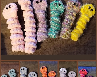 May include: A collection of handmade crochet worm toys in various colors including light pink, lavender, teal, yellow, blue, orange, gray, and red. Each worm features a spiral-shaped body made of soft yarn and two small black bead eyes.