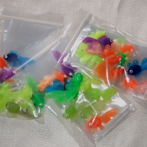 May include: A variety of colorful plastic toy fish in clear plastic bags. The fish are in various colors, including green, blue, orange, purple, and yellow.
