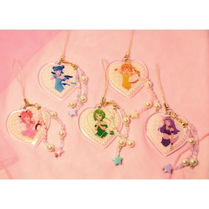 May include: A collection of heart-shaped acrylic charms featuring anime-style illustrations of female characters. Each charm has a lace-like border and is adorned with pearl and star-shaped beads. The charms are in various colors, including pink, blue, green, orange, and purple.