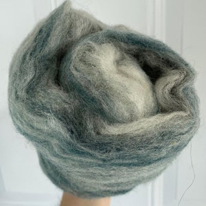 May include: A bundle of teal and white wool roving. The wool is soft and fluffy, and it is perfect for felting or spinning.